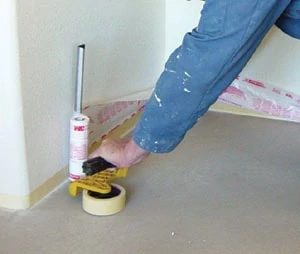 Over a layer of medium-tack masking tape close to the floor, a masking machine applies tape and thin plastic, which is then unfolded up the wall to a height of 2 feet and tacked into place.