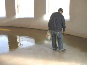 A worker sprays a heavy coat of stain on a cleaned and dry floor. This living room reacted strongly and required only one application of stain.