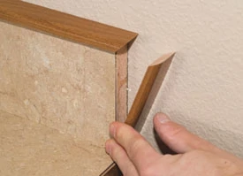 We machine and fasten a small wood cap that slightly overhangs the laminate back splash.