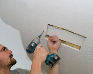 You can hold on to the backer board with one hand, while fastening it to the drywall with the other.