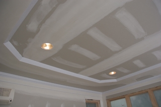 Joint compound is used to conceal the stapled edge of the bead. The angled edge does not need to be coated. After priming, the edge against the upper ceiling can be caulked for a more perfect blend into the upper ceiling.