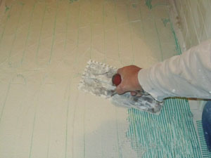 If installing the mesh with thin-set mortar, use a scraper or a flat trowel to spread a layer of the product until the heating cable and guides are completely covered. Allow the thin-set to set according to the product's instructions. 