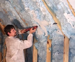 An installer uses a long reciprocating blade to cut the expanded SPF flush with the wall studs. 