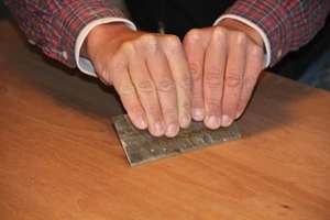 Hold the cabinet scraper with both hands at a low angle to the wood. The shape of the burr on the scraper allows approximately 0.02 millimeters of material to be removed at a time. 