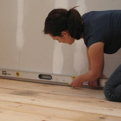 Find the highest spot in the floor where the cabinets will sit, then register your level line. The longer the level, the easier it is to get an accurate mark. 