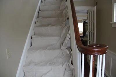 A canvas drop cloth makes a flexible and reusable protective cover for stairs surfaced with wood or carpet.