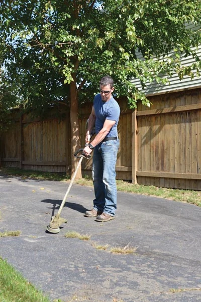For weeds and grass in driveway cracks, try to pull out the plants by the root. If you can't get an adequate grip, then cut them down with a string trimmer and apply weed killer to the root system.