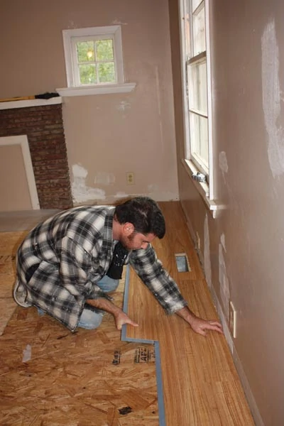 The adhesive strip along the long edge is then carefully pressed into place. Pro remodeler Richie Hamilton installs the flooring.