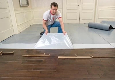 Lay out the Elastilon membrane on the subfloor, peel off the protective film, and press your wood flooring onto the sticky surface.