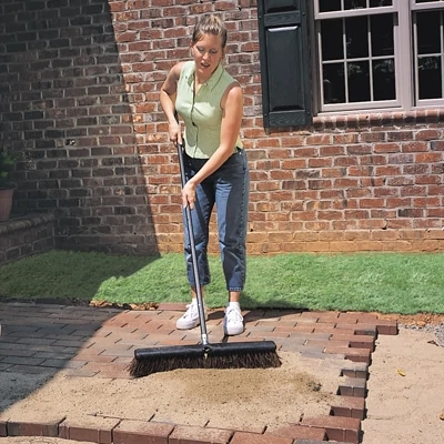 After placing the paver stones over the sand bed in your preferred pattern, sweep sand over the installation to fill the joints between pavers. 
