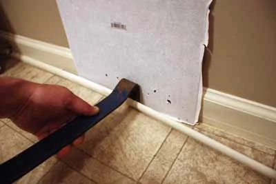 I open the joint with a paint scraper and then slip my flat bar inside to pry off the molding. A spare piece of tile protects the baseboard.