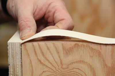 To apply veneer tape between two existing pieces, heat the starting joint so it doesn’t separate. Leave the opposite end of the tape unheated. Cut the end square and 1/64” longer than the seam. Bow up your tape and tuck your seam tight to the edge of the intersecting tape. 