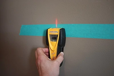 Locate and mark the studs. I make pencil marks on the painter’s tape to keep the walls clean. 