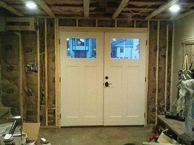 Short cripple studs fit between the header and top plate. Doubled wall studs frame each side of the door jamb. The wall is then insulated with fiberglass batts. 