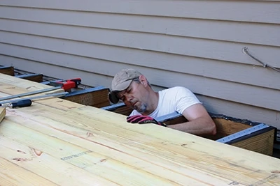 In tight spots, support your weight with an arm draped over a joist while you fasten the nearest board.