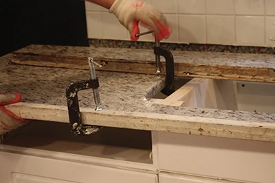 NOte the angle-iron bracing clamped across the length of the countertop to stabilize and reinforce its shape. This is kparticularly important for the section with the sink cut-out, which has a weakened center area since the granite is missing. 