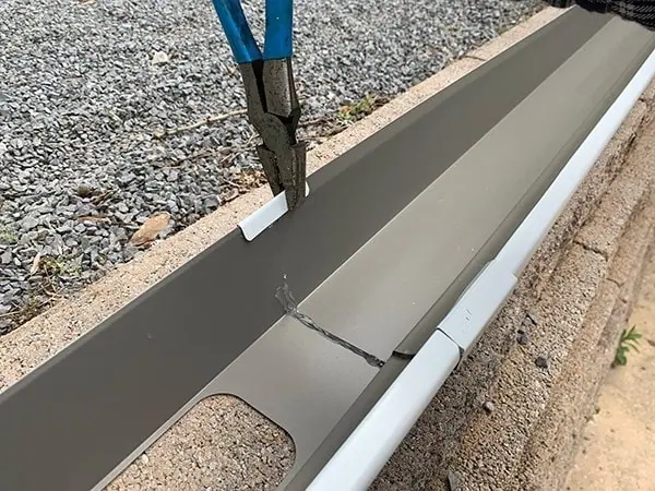 After they've been wrapped over the joint, the seamers hook over the front and back edges of the gutter, where they get crimped into place with pliers.