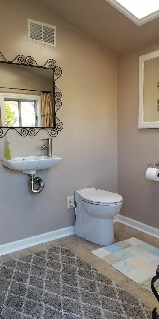 The half-bath inside the converted storage shed, showing the self-contained Sanicompact, dual-flush macerating toilet on the right, next to the small hand-washing sink.
